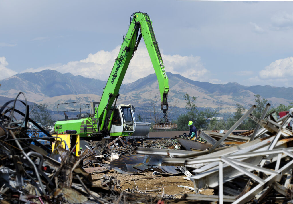 A recycling crane lifting a pile of scrap metal with a magnet at a recycling facility.